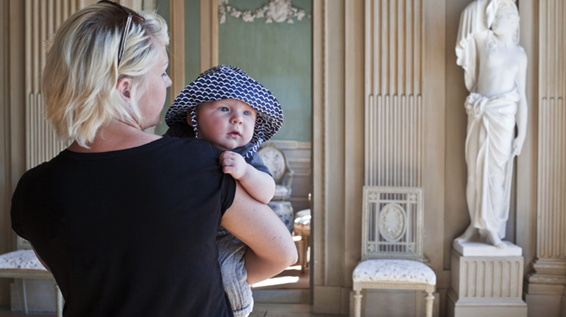 Bebis i en mammas famn i ett av slottets salar som tittar över mammans axel.