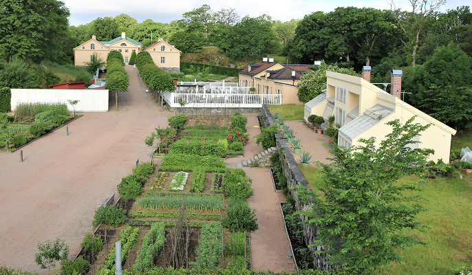 Fågelperspektiv över Gunnebo köksträdgård med sina grönskande odlingar med slottets byggnader i förgrunden.