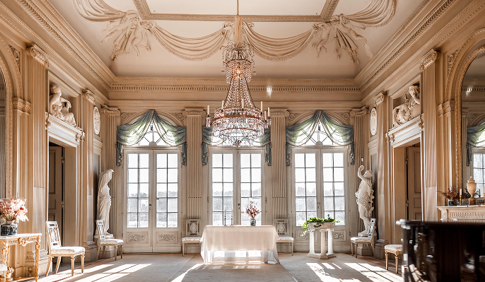 En ståtlig, ljus slottsalong på Gunnebo, med kristallkrona, dubbeldörrar och annan tidsenlig interiör.